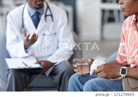 Side view close up of unrecognizable African American woman holding glass of water and tissue during difficult consultation at doctors office, copy space Side view close up of unrecognizable African American woman holding glass of water and tissue during difficult consultation at doctors office, copy space 121270605