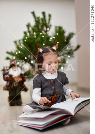 Cute little child girl reads Christmas stories and fairy tales near the Christmas tree at home Cute little child girl reads Christmas stories and fairy tales near the Christmas tree at home 121271046