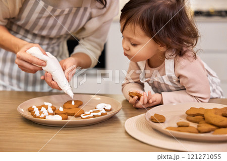 happy mother and little child girl decorating a traditional gingerbread in kitchen at home happy mother and little child girl decorating a traditional gingerbread in kitchen at home 121271055