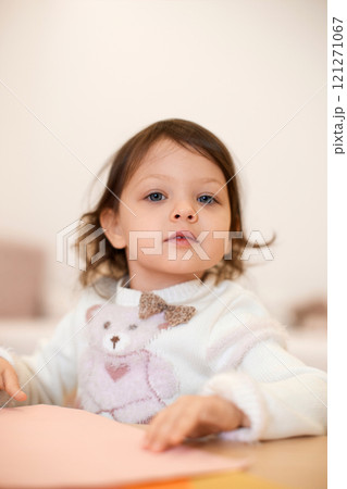 little child girl holding multi-color paper while sitting by table at home 121271067
