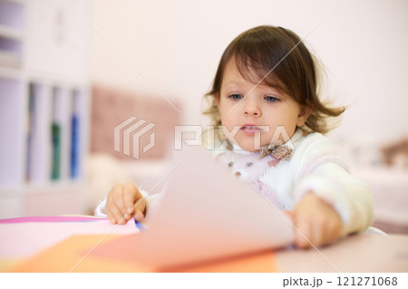 little child girl holding multi-color paper while sitting by table at home, Children creativity 121271068
