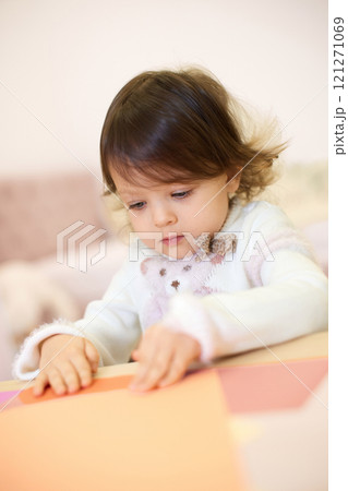 little child girl holding multi-color paper while sitting by table at home 121271069
