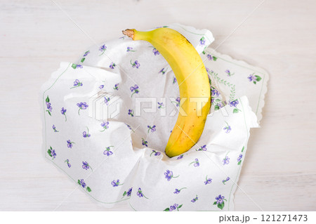 Ripe banana nestled in a floral patterned napkin on a white wooden table. 121271473