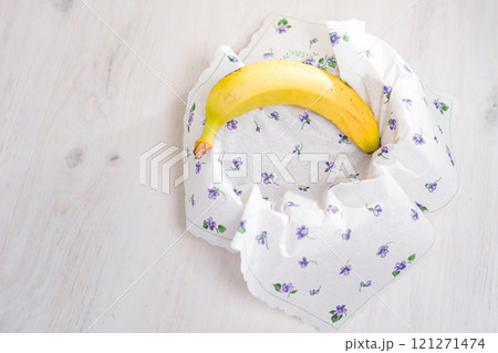 Ripe banana nestled in a floral napkin on a white wooden table. 121271474