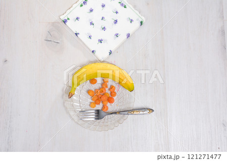 Banana, yellow raspberries, and a fork on a glass plate with a napkin. 121271477