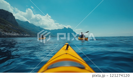 Two kayakers paddle through calm blue waters near rugged mountains in a tranquil coastal setting Two kayakers paddle through calm blue waters near rugged mountains in a tranquil coastal setting 121274120