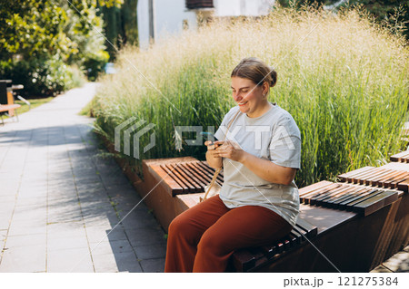 Happy woman chatting on phone and relaxing on the bench outdoors. Urban people concept. Smiling woman text messaging on smart phone at sunny day. Happy woman chatting on phone and relaxing on the bench outdoors. Urban people concept. Smiling woman text messaging on smart phone at sunny day. 121275384