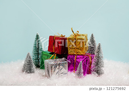 colorful, shiny gift boxes is arranged on artificial snow, surrounded by small, glittery miniature Christmas trees 121275692