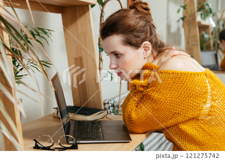 happy young woman is sitting at desk in home office, looking at laptop screen studying 121275742