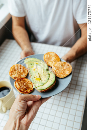 man has breakfast at home in kitchen. plate with avocado toast, pancakes and black coffee man has breakfast at home in kitchen. plate with avocado toast, pancakes and black coffee 121275774