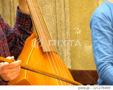 Musician Plays a Viola Da Gamba Using a Bow in a Historical Courtyard During a Sunny Afternoon 121276009