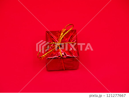 A red gift box with a gold ribbon on a striking red background 121277667