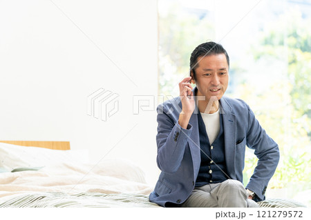 ベッドに座ってスマホで話すミドル男性 ベッドに座ってスマホで話すミドル男性 121279572