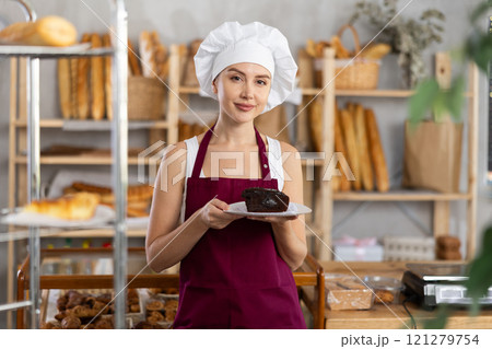 Young saleswoman holding piece of pastry in paper plate Young saleswoman holding piece of pastry in paper plate 121279754