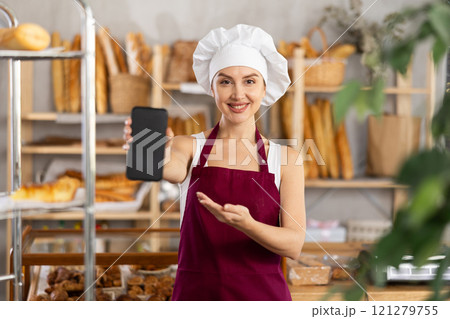Young saleswoman displays a mobile application in bakery shop Young saleswoman displays a mobile application in bakery shop 121279755