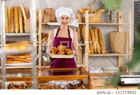 Young saleswoman displays croissants in square wicker basket Young saleswoman displays croissants in square wicker basket 121279802
