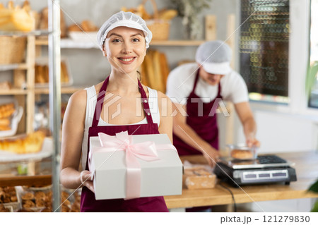 Cheerful female baker holding gift box with baked treats 121279830