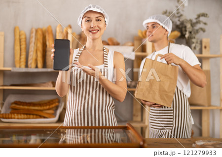 Young woman and guy sellers with bag and smartphone in bakery 121279933