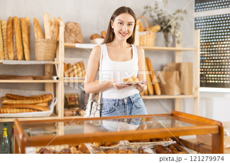 Satisfied female customer selects fresh croissants at display window of bakery Satisfied female customer selects fresh croissants at display window of bakery 121279974