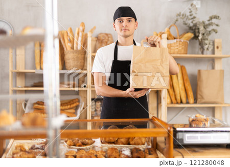 Dedicated young baker holding out bag of freshly baked goods Dedicated young baker holding out bag of freshly baked goods 121280048