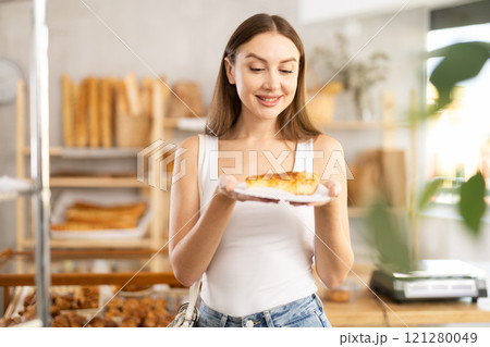 Satisfied female customer selects fresh croissants at display window of bakery 121280049
