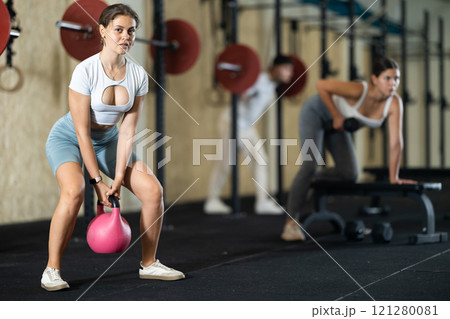 Young girl doing exercises with kettlebell near other people in crossfit gym Young girl doing exercises with kettlebell near other people in crossfit gym 121280081