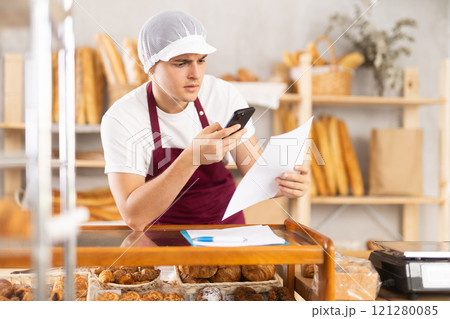 Focused young bakery manager organizing orders with smartphone 121280085