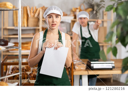 Frustrated female bakery worker holding paper amid workplace argument 121280216