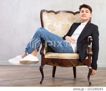 Smiling young guy posing while sitting in chair Smiling young guy posing while sitting in chair 121280261