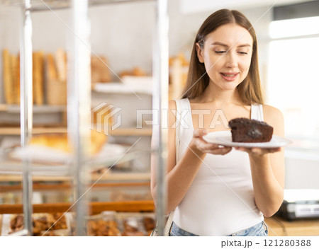 Positive young girl holding pastry on paper plate in bakery 121280388