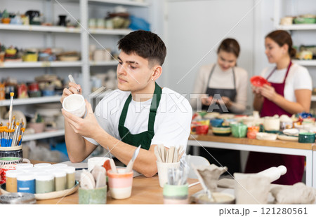 Young man painting pottery in workshop 121280561