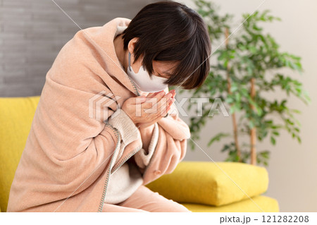 冬の部屋で咳き込むマスクをつけたミドル〜シニア女性 121282208