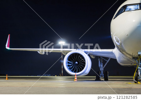 Front view of a white passenger airplane connected to an external power supply on an airport night apron 121282585