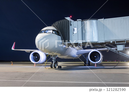 A white passenger jet plane at the air bridge connected to an external power supply on an airport night apron 121282590