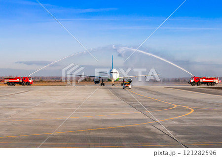 Water salute by fire truck at the airport for first visit passenger airplane. The plane moves behind the Follow-me-Car 121282596