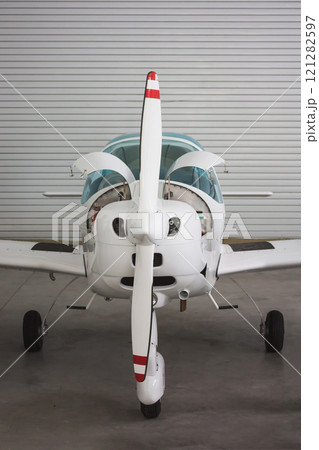 Close front view of a small white sports plane in a hangar. The aircraft has an open engine 121282597