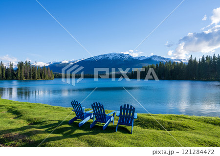 Jasper National Park summer landscape, Alberta, Canada. Adirondack chairs on lakeside of the Beauvert Lake (Lac Beauvert). Snowcapped Whistlers Peak mountain in the background. Jasper National Park summer landscape, Alberta, Canada. Adirondack chairs on lakeside of the Beauvert Lake (Lac Beauvert). Snowcapped Whistlers Peak mountain in the background. 121284472