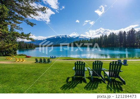 Jasper National Park summer landscape, Alberta, Canada. Adirondack chairs on lakeside of the Beauvert Lake (Lac Beauvert). Snowcapped Whistlers Peak mountain in the background. Jasper National Park summer landscape, Alberta, Canada. Adirondack chairs on lakeside of the Beauvert Lake (Lac Beauvert). Snowcapped Whistlers Peak mountain in the background. 121284473