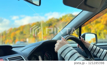 紅葉で色づいた山道をドライブする若い女性 ハンドルを握る手 紅葉で色づいた山道をドライブする若い女性 ハンドルを握る手 121285398