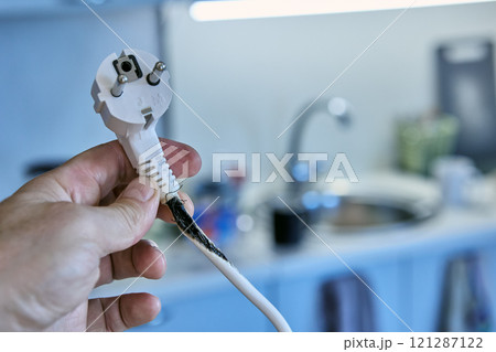 Burnt out cable with an electrical plug in hand of user who has overloaded an extension cord with tee. 121287122