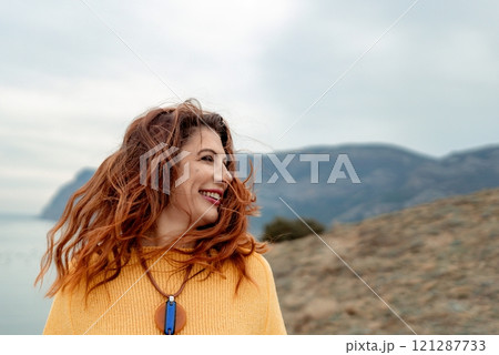 Portrait windswept hair happy woman against a backdrop of mountains and sea. Daylight illuminates the tranquil outdoor setting Portrait windswept hair happy woman against a backdrop of mountains and sea. Daylight illuminates the tranquil outdoor setting 121287733