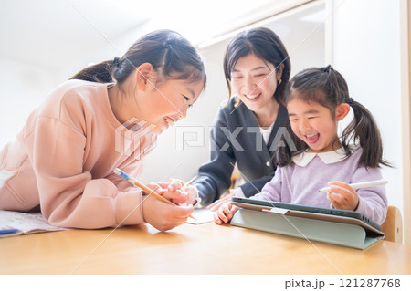 逆光の中、勉強や宿題をみるお母さんや塾の先生 小学生低学年の笑顔の子供「タブレットでも勉強楽しい」ク 逆光の中、勉強や宿題をみるお母さんや塾の先生 小学生低学年の笑顔の子供「タブレットでも勉強楽しい」ク 121287768