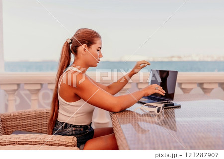 Woman coffee cafe laptop sea. Female freelancer using laptop on coffee break in modern cafe with sea view in the morning 121287907