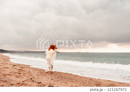 Women sea walk friendship spring. Two girlfriends, redhead and blonde, middle-aged walk along the sandy beach of the sea, dressed in white clothes. Against the backdrop of a cloudy sky and the winter Women sea walk friendship spring. Two girlfriends, redhead and blonde, middle-aged walk along the sandy beach of the sea, dressed in white clothes. Against the backdrop of a cloudy sky and the winter 121287972