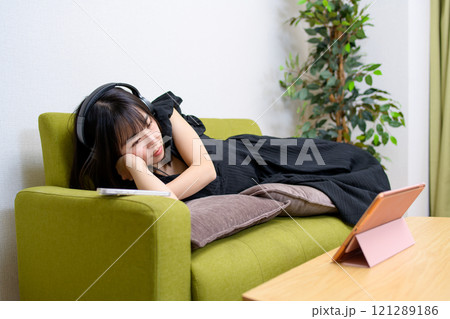 リビングでヘッドフォンをつけタブレットで動画を見る若い女性 動画視聴 ライブ実況 中継 寝転ぶ リビングでヘッドフォンをつけタブレットで動画を見る若い女性 動画視聴 ライブ実況 中継 寝転ぶ 121289186