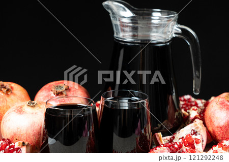 Pomegranate juice in jug and glasses among pomegranates, black background. Pomegranate juice in jug and glasses among pomegranates, black background. 121292248