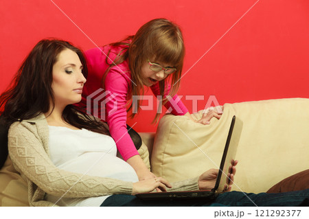Pregnant woman and daughter sitting with laptop Pregnant woman and daughter sitting with laptop 121292377