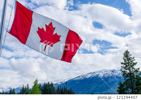 Close up of National Flag of Canada with trees and snow-capped mountains in the background. Close up of National Flag of Canada with trees and snow-capped mountains in the background. 121294407