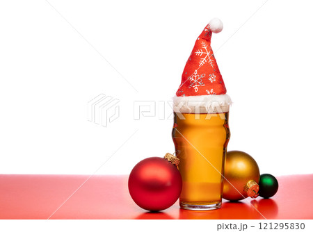 Festive beer glass with a Santa hat surrounded by colorful Christmas baubles on a red background 121295830