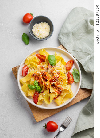 Flat lay of tagliatelle pasta with tomato sauce, basil and parmesan cheese in a plate on a  board  121297550